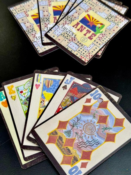 Arizona ANTE cards fanned with art backs in background and illustrated face cards in front