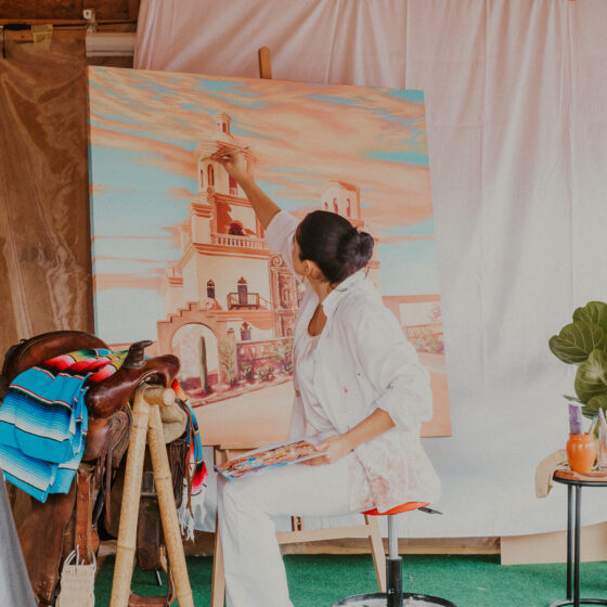 Camila Ibarra paints a majestic castle scene on a large canvas at her studio, focused and absorbed in her art.