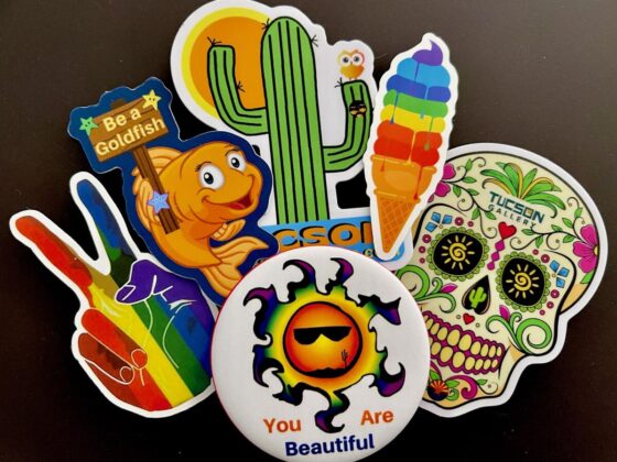 GayTucson "You Are Beautiful" magnetic button and five colorful Pride stickers including a peace sign in rainbow colors, Be a Goldfish sticker, Tucson Gallery cactus sticker, melting ice cream in rainbow colors, and Tucson Gallery sugar skull sticker.