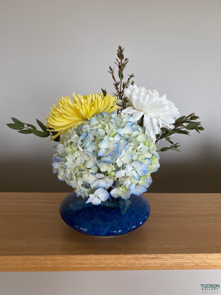 Ikebana flower arrangement with hydrangea and chrysanthemums in a blue vase on a wooden shelf