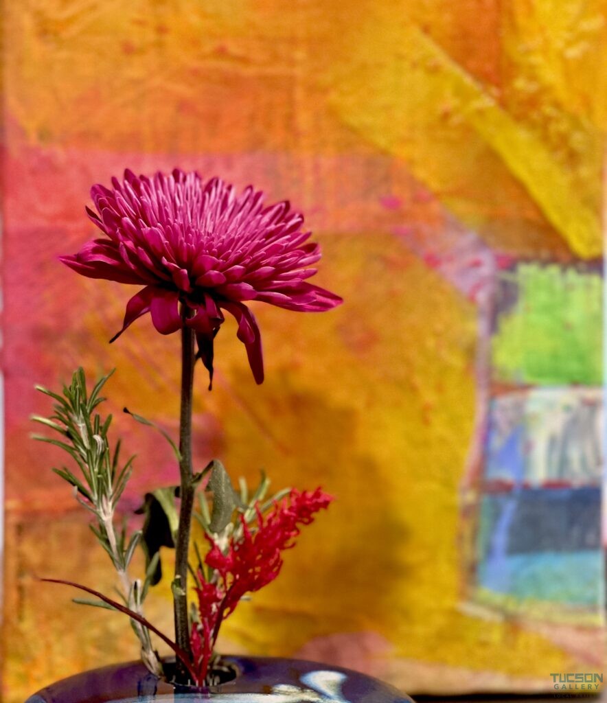 Vibrant magenta chrysanthemum in a black ikebana vase with bold abstract backdrop