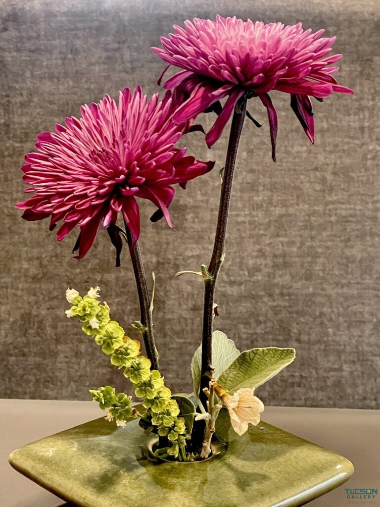 Close-up of dual chrysanthemums in green vase against textured gray background