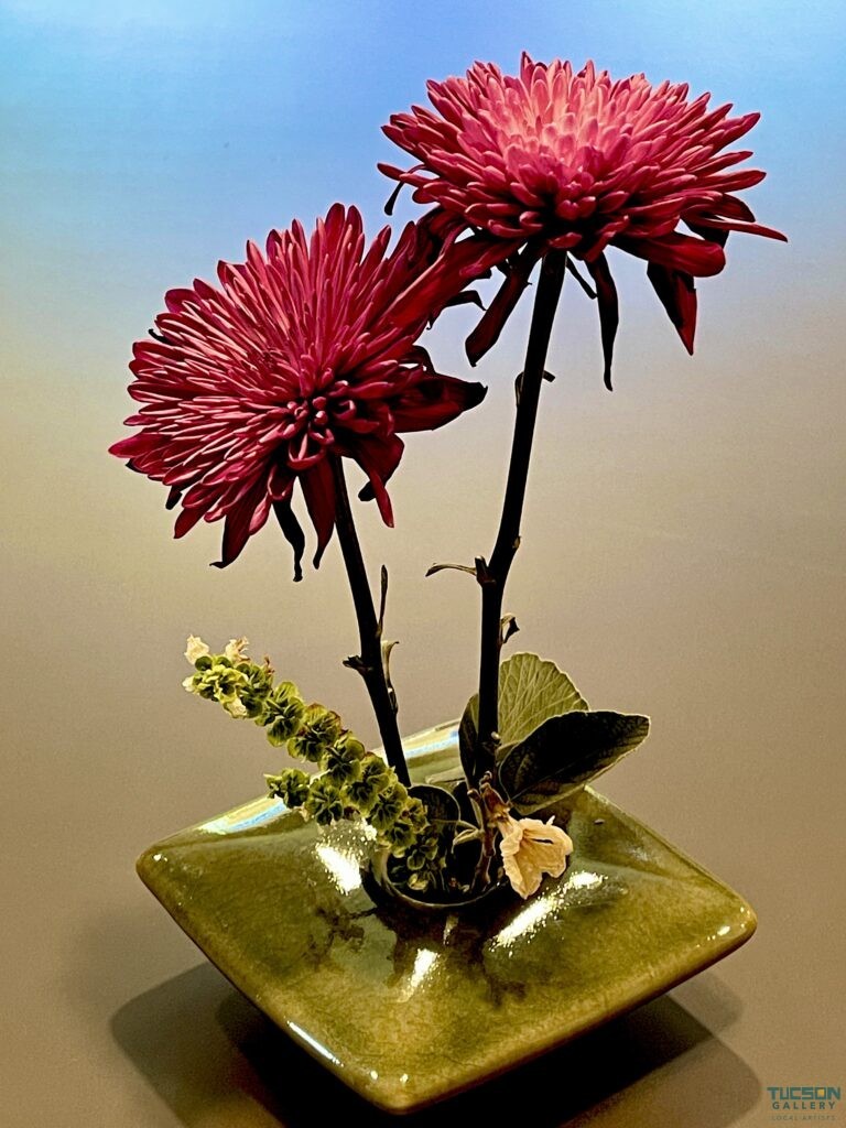 Artistic ikebana with magenta chrysanthemums and desert herbs in a green vase