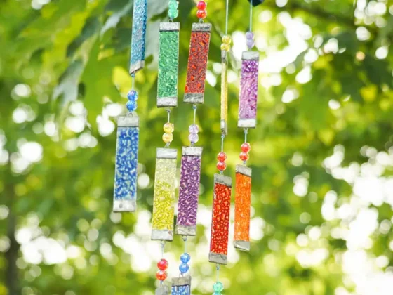 Close-up of rainbow textured tiered glass wind chime hanging outdoors, showing layered strands of colorful glass panels and beads