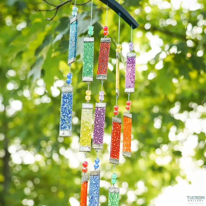 Close-up of rainbow textured tiered glass wind chime hanging outdoors, showing layered strands of colorful glass panels and beads