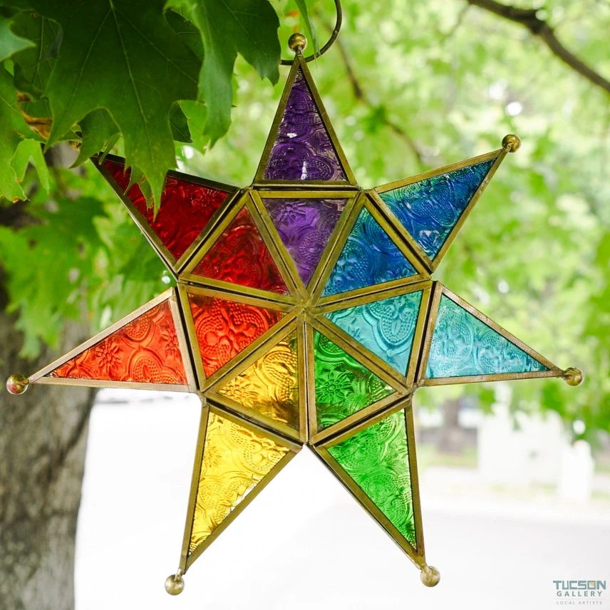 Rainbow seven-point star tealight lantern hanging outdoors from a hook, with green leaves in the background