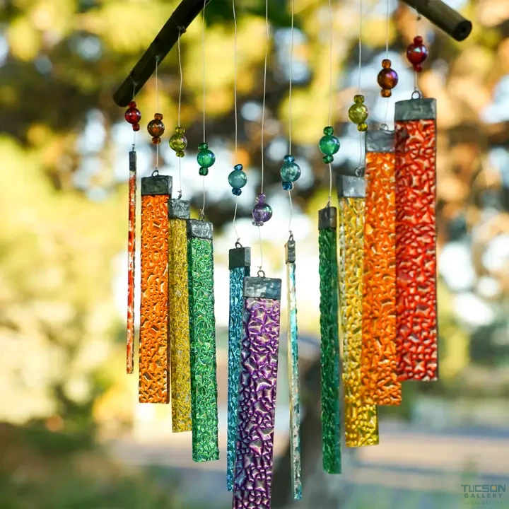 Rainbow textured glass wind chime hanging from a branch with green leaves in the background