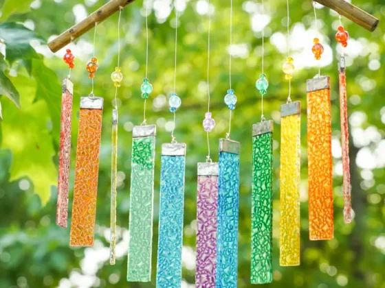 Rainbow textured glass wind chime hanging from a branch with green leaves in the background