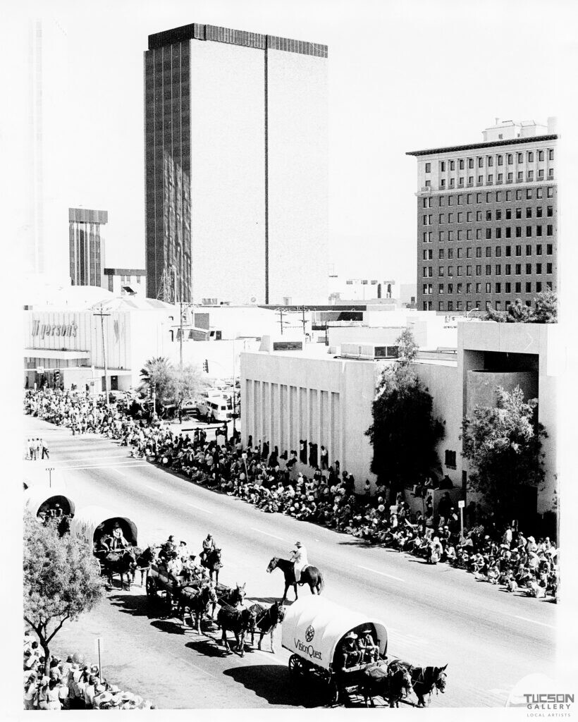 Horse-drawn wagons in the Tucson Rodeo Parade pass crowds and downtown buildings during the 1980s.